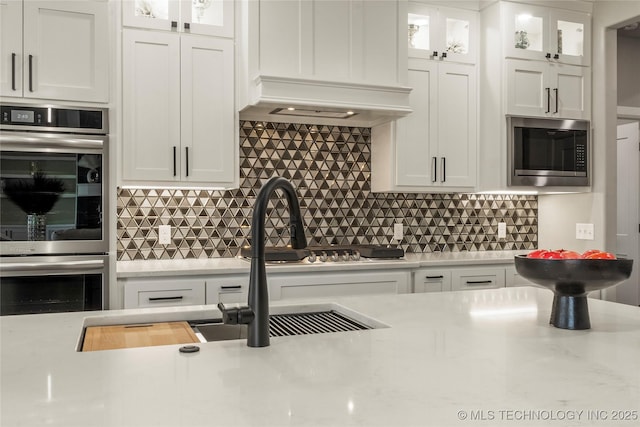 kitchen featuring stainless steel appliances, custom range hood, white cabinets, and decorative backsplash