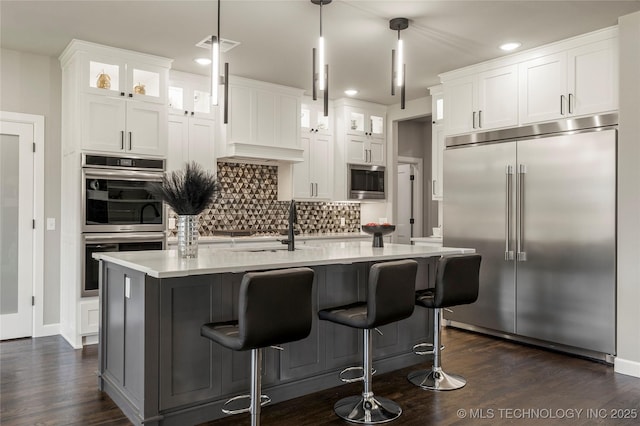 kitchen featuring white cabinetry, pendant lighting, a kitchen island with sink, and built in appliances