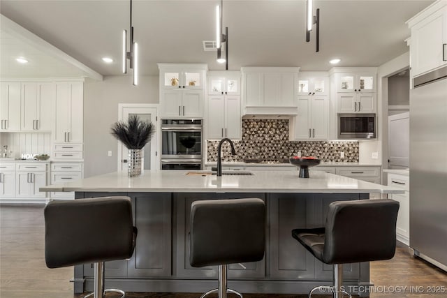 kitchen with white cabinetry, built in appliances, and a center island with sink