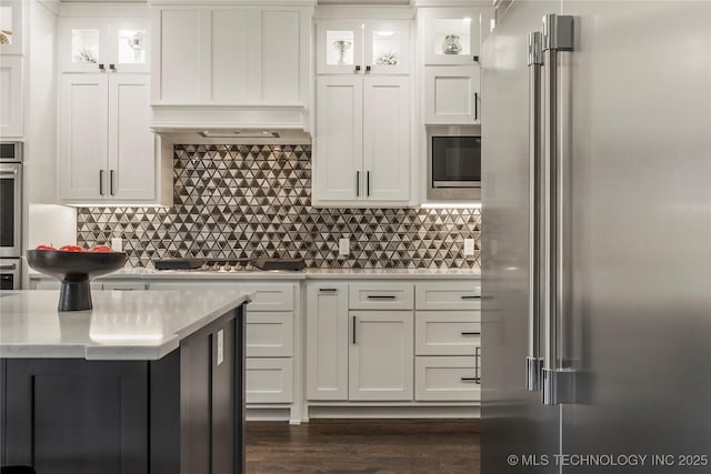 kitchen with stainless steel appliances, premium range hood, white cabinets, and backsplash