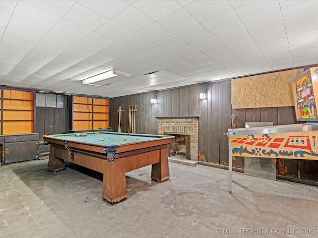 game room with billiards, a fireplace, wooden walls, and concrete flooring