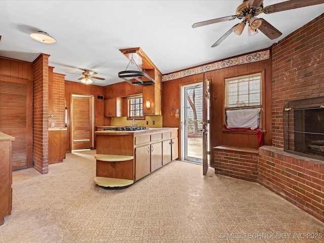 kitchen with ceiling fan, a fireplace, brick wall, decorative light fixtures, and wood walls