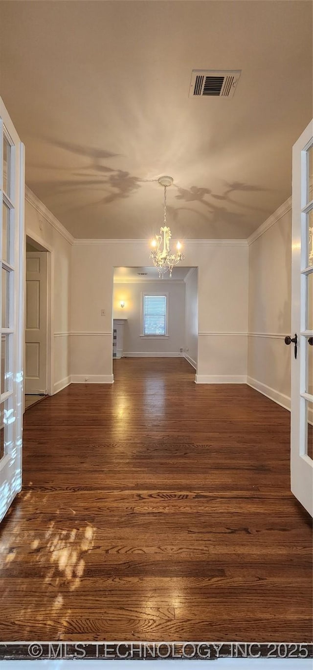 spare room with a notable chandelier, ornamental molding, dark hardwood / wood-style floors, and french doors