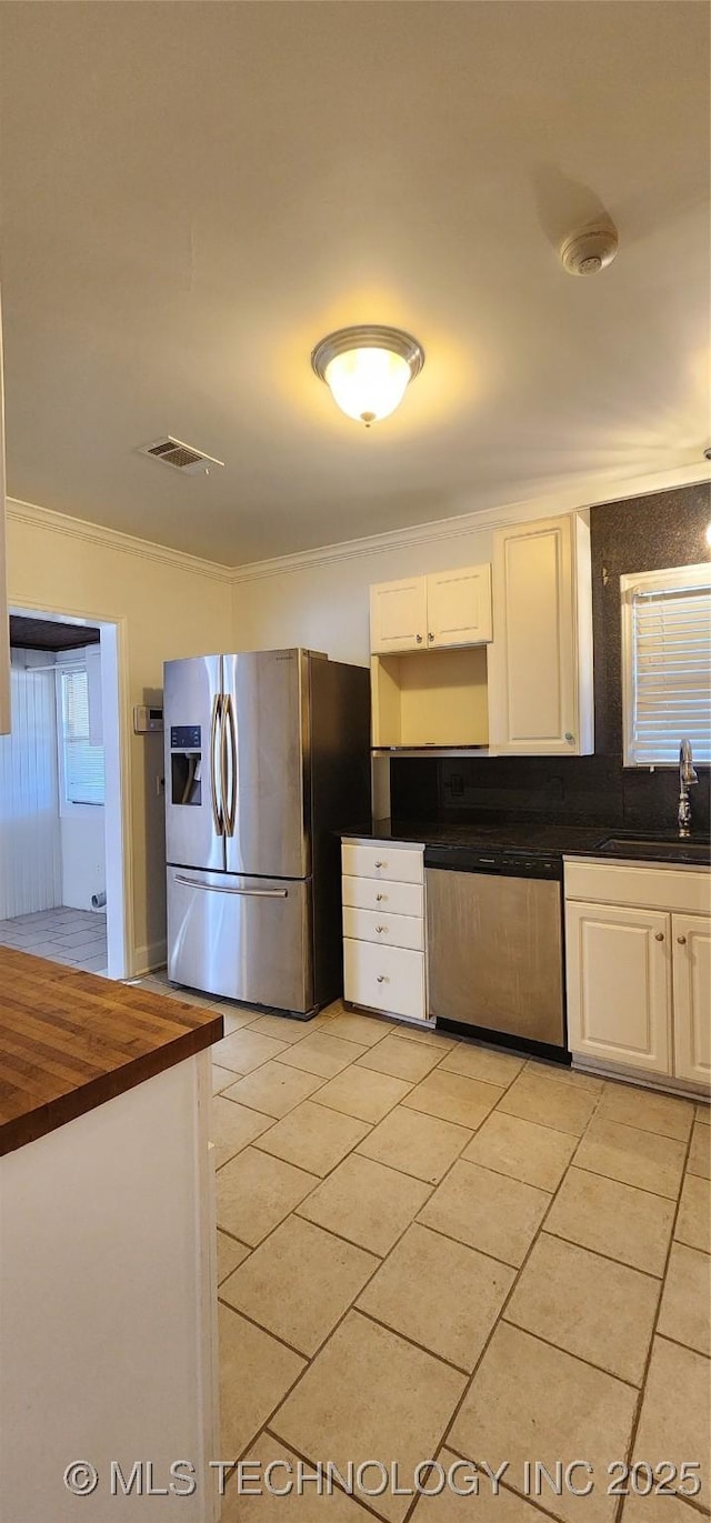 kitchen with sink, white cabinetry, light tile patterned floors, ornamental molding, and appliances with stainless steel finishes