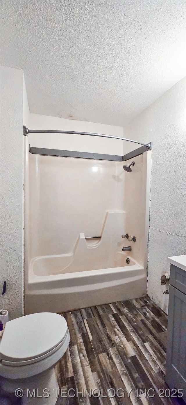 full bathroom with hardwood / wood-style floors, a textured ceiling, toilet, and washtub / shower combination