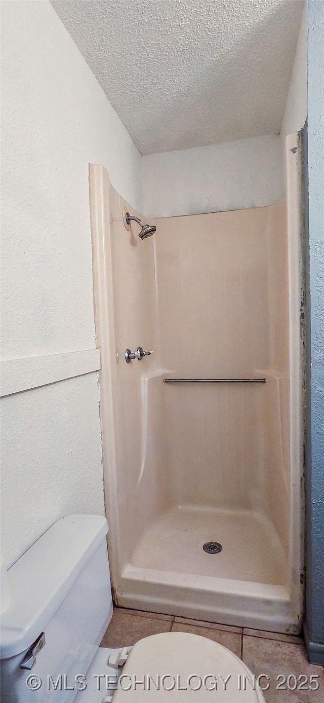 bathroom with tile patterned flooring, toilet, a textured ceiling, and walk in shower