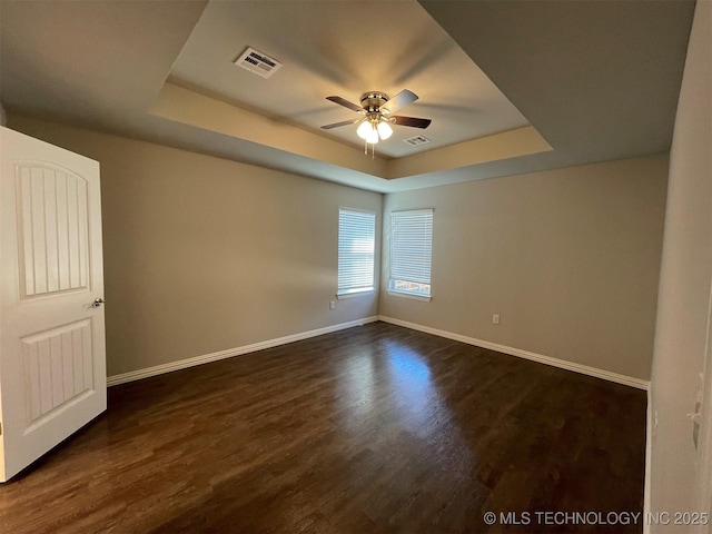 unfurnished room featuring a tray ceiling, dark wood-type flooring, and ceiling fan