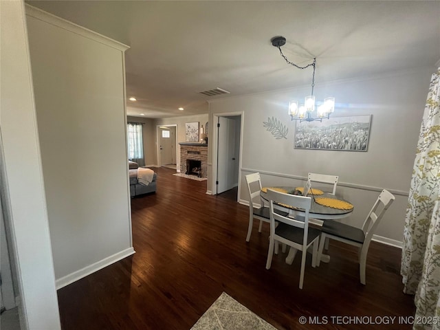 dining area with ornamental molding, a brick fireplace, dark wood-type flooring, and a chandelier