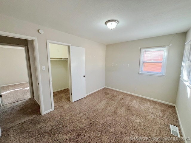 unfurnished bedroom with a spacious closet, a closet, and carpet flooring