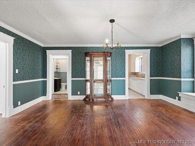 empty room featuring hardwood / wood-style flooring, ornamental molding, an inviting chandelier, and a textured ceiling