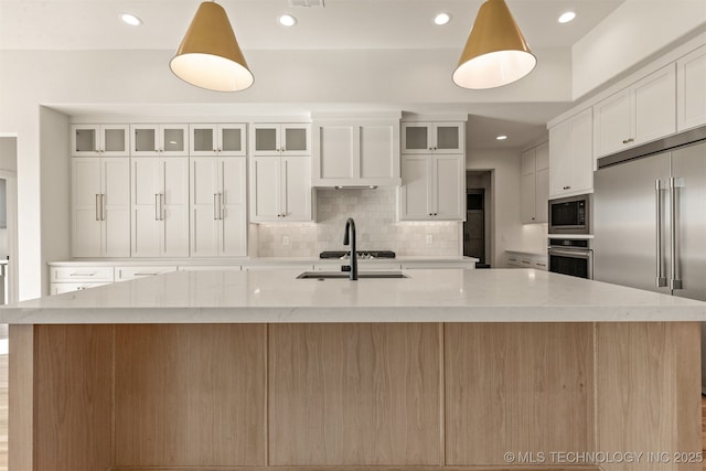 kitchen featuring white cabinetry, built in appliances, sink, and a large island with sink