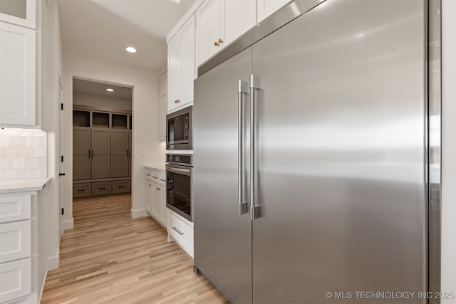 kitchen featuring built in appliances, white cabinetry, and light wood-type flooring