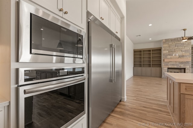 kitchen featuring a stone fireplace, built in features, white cabinets, built in appliances, and light wood-type flooring