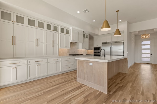 kitchen with white cabinetry, built in appliances, a center island with sink, and backsplash