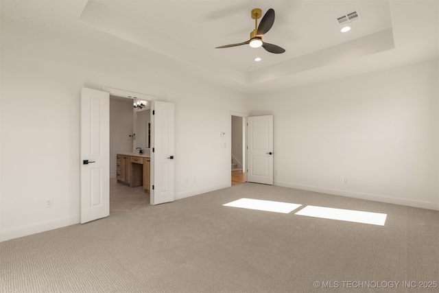 unfurnished bedroom with ensuite bath, light carpet, ceiling fan, and a tray ceiling