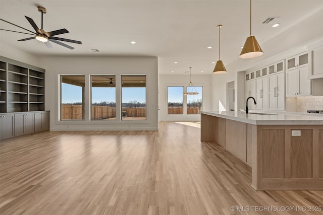 kitchen with a large island, light hardwood / wood-style flooring, hanging light fixtures, white cabinets, and decorative backsplash