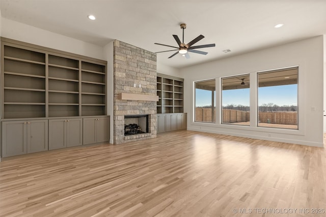 unfurnished living room with a stone fireplace, light hardwood / wood-style flooring, built in features, and ceiling fan