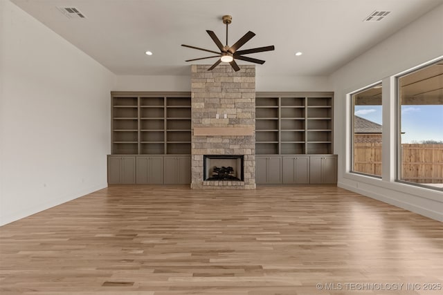 unfurnished living room featuring a stone fireplace, light wood-type flooring, and built in shelves