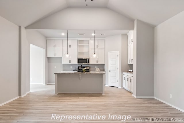 kitchen with lofted ceiling, light stone counters, appliances with stainless steel finishes, a kitchen island with sink, and white cabinets