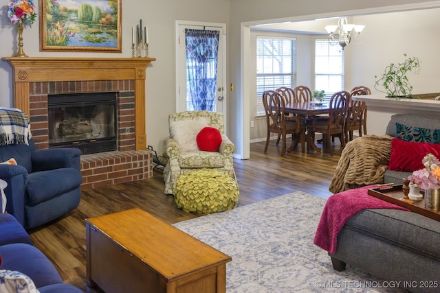 living room with dark hardwood / wood-style flooring, a chandelier, and a brick fireplace