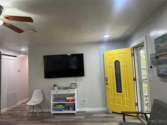 living room with wood-type flooring, a barn door, a textured ceiling, and ceiling fan