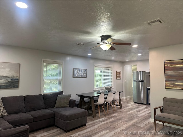 living room with ceiling fan, light wood-type flooring, a wealth of natural light, and a textured ceiling