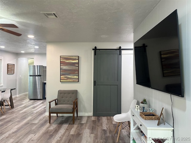 interior space featuring a textured ceiling, wood-type flooring, a barn door, and ceiling fan