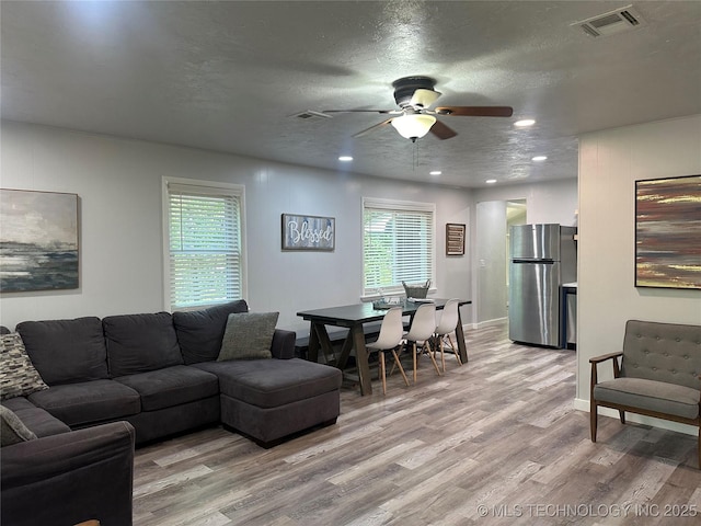 living room with ceiling fan, plenty of natural light, light hardwood / wood-style floors, and a textured ceiling