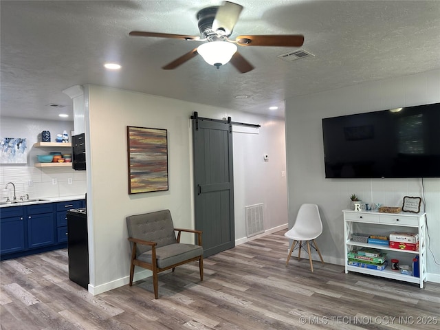 sitting room featuring sink, a textured ceiling, hardwood / wood-style flooring, ceiling fan, and a barn door