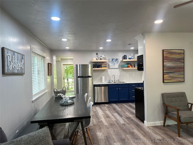 kitchen with blue cabinets, sink, tasteful backsplash, light hardwood / wood-style flooring, and stainless steel appliances