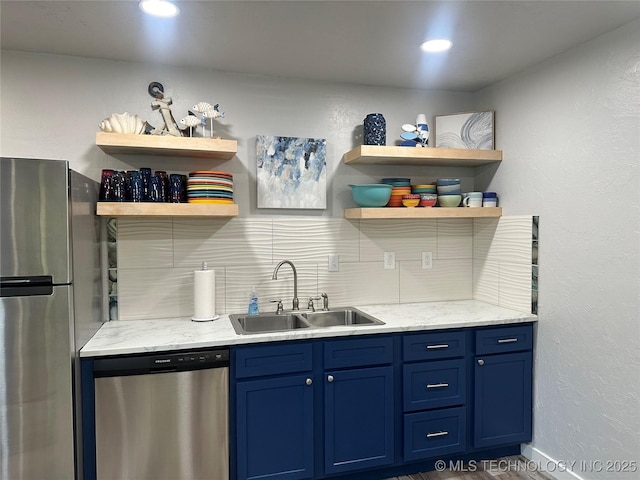 kitchen with light stone counters, sink, stainless steel appliances, and blue cabinetry