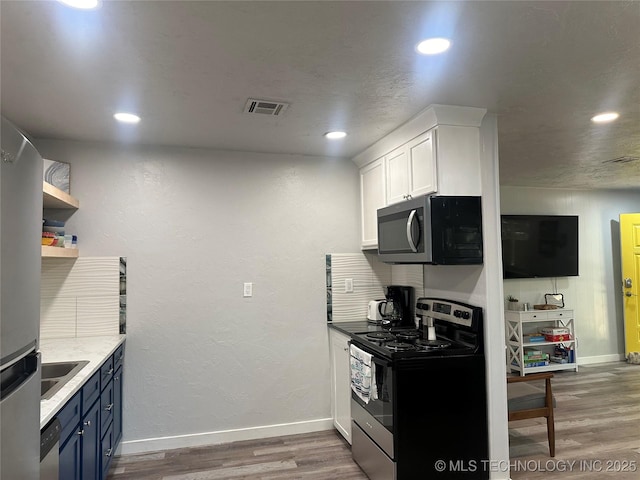 kitchen featuring appliances with stainless steel finishes, blue cabinets, white cabinets, light stone countertops, and dark wood-type flooring