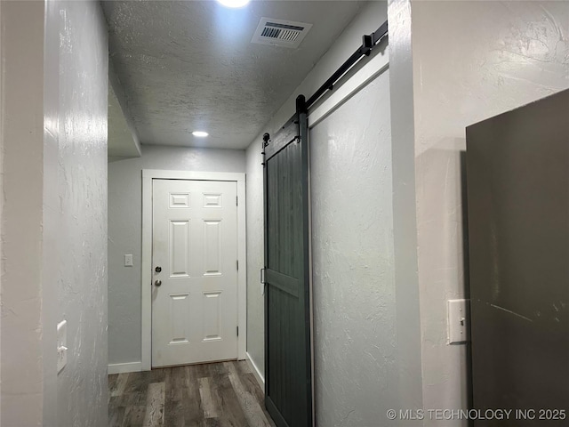 corridor featuring wood-type flooring, a barn door, and a textured ceiling