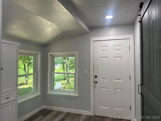 doorway to outside with dark hardwood / wood-style floors, a barn door, vaulted ceiling, and a textured ceiling