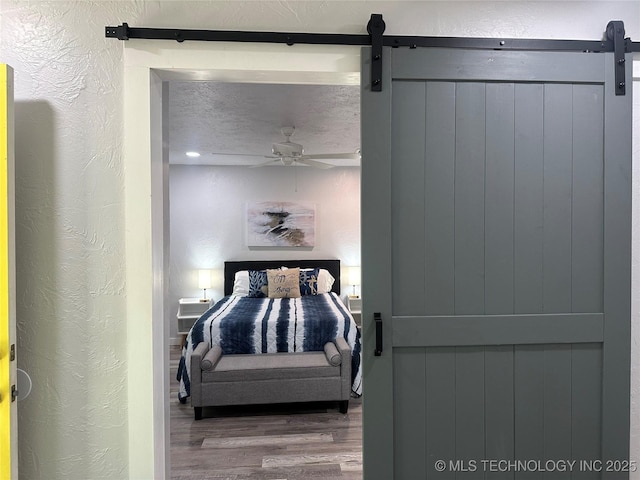 bedroom featuring a barn door, hardwood / wood-style floors, a textured ceiling, and ceiling fan