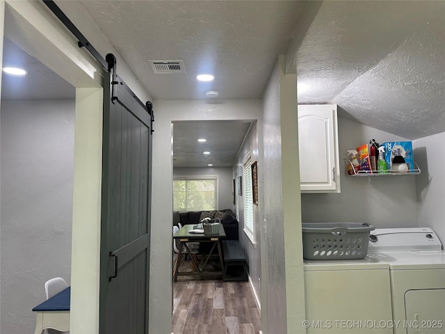 laundry room featuring cabinets, wood-type flooring, washer and dryer, a textured ceiling, and a barn door