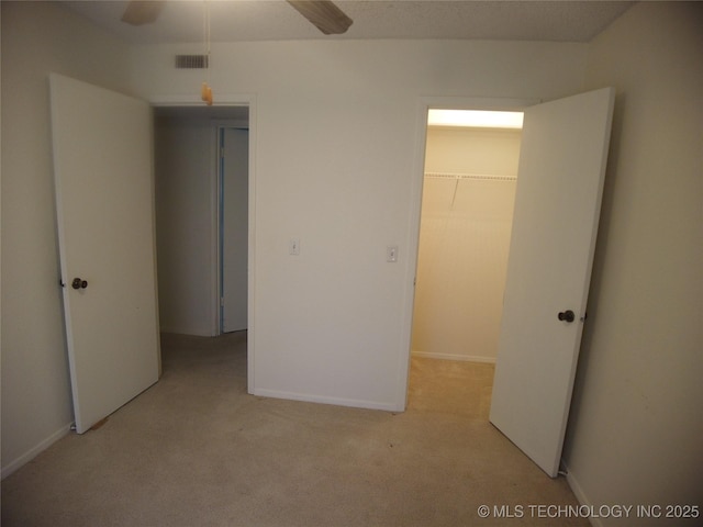 unfurnished bedroom with a walk in closet, light carpet, ceiling fan, and a closet