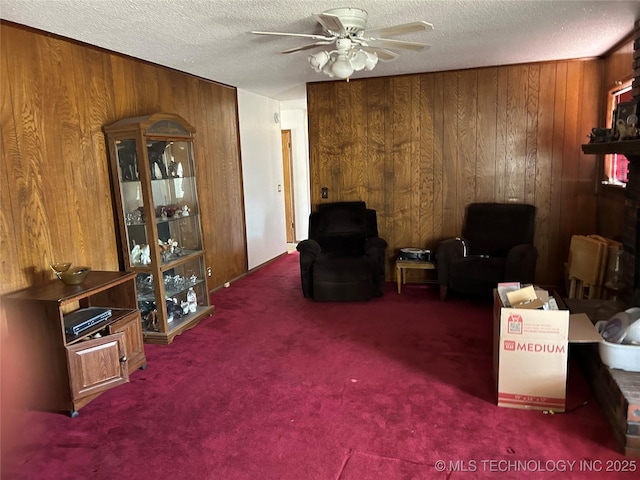 sitting room featuring carpet flooring, ceiling fan, wooden walls, and a textured ceiling