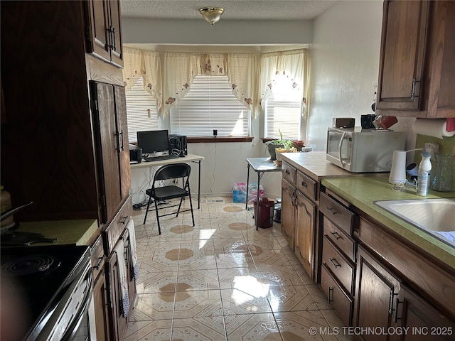 kitchen featuring stainless steel electric stove, sink, a textured ceiling, and light tile patterned floors