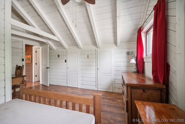 bedroom with dark hardwood / wood-style flooring, vaulted ceiling with beams, ceiling fan, and wood walls