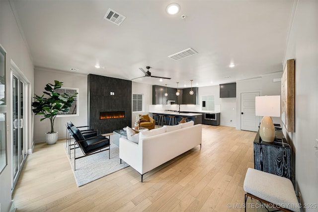 living room featuring a tiled fireplace, crown molding, ceiling fan, and light wood-type flooring