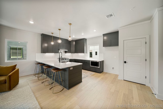 kitchen featuring stainless steel microwave, decorative light fixtures, sink, a kitchen bar, and light wood-type flooring