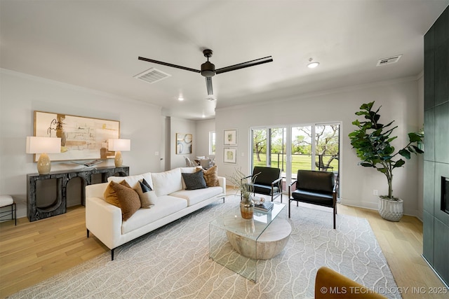 living room featuring ceiling fan, ornamental molding, a fireplace, and light wood-type flooring