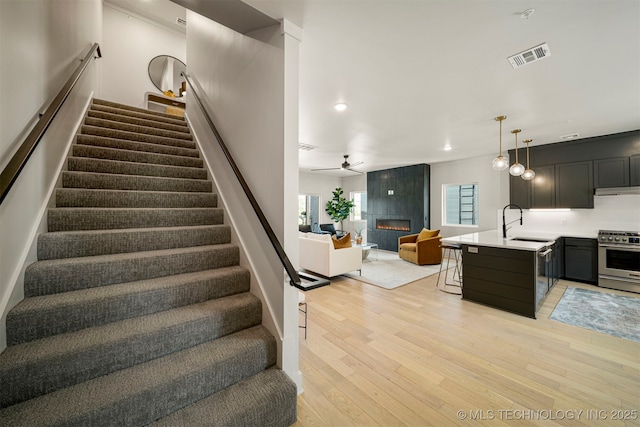 stairs with a tiled fireplace, hardwood / wood-style floors, sink, and ceiling fan