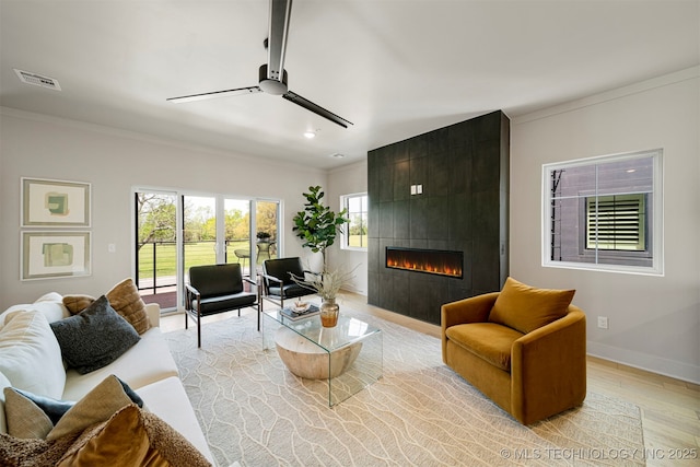 living room featuring a tiled fireplace, crown molding, ceiling fan, and light wood-type flooring