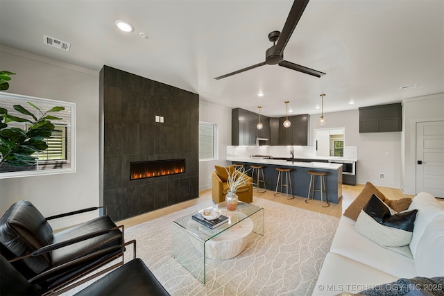 living room featuring a tiled fireplace, ceiling fan, a wealth of natural light, and light wood-type flooring