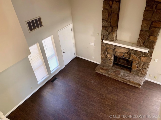 unfurnished living room with a stone fireplace, dark hardwood / wood-style floors, and a towering ceiling