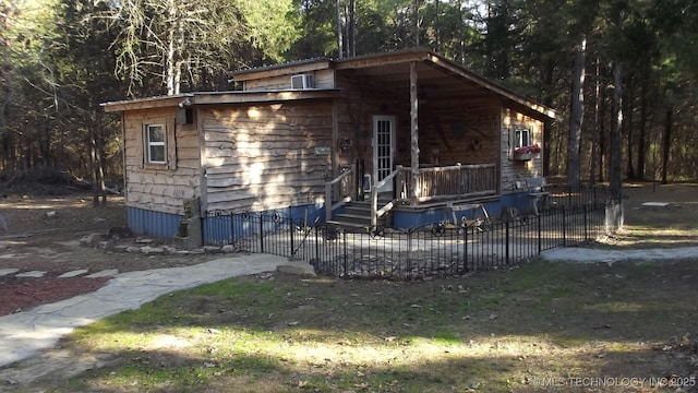 view of front facade featuring fence, cooling unit, and a view of trees