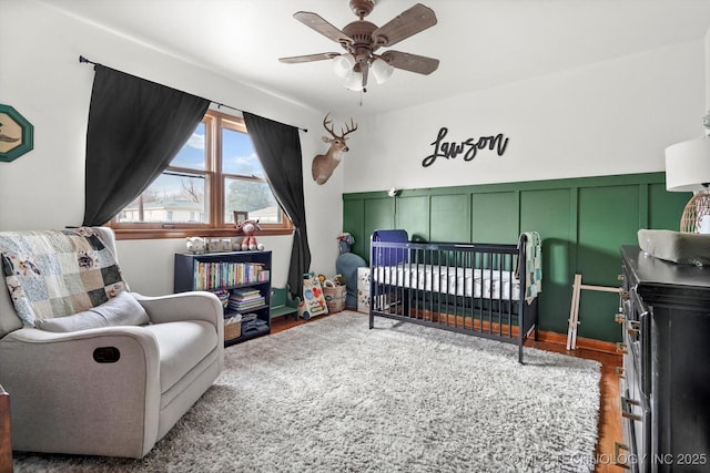 bedroom featuring wood-type flooring, a nursery area, and ceiling fan