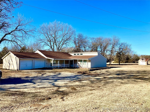 view of front of property featuring a porch, an attached garage, a storage shed, an outdoor structure, and driveway